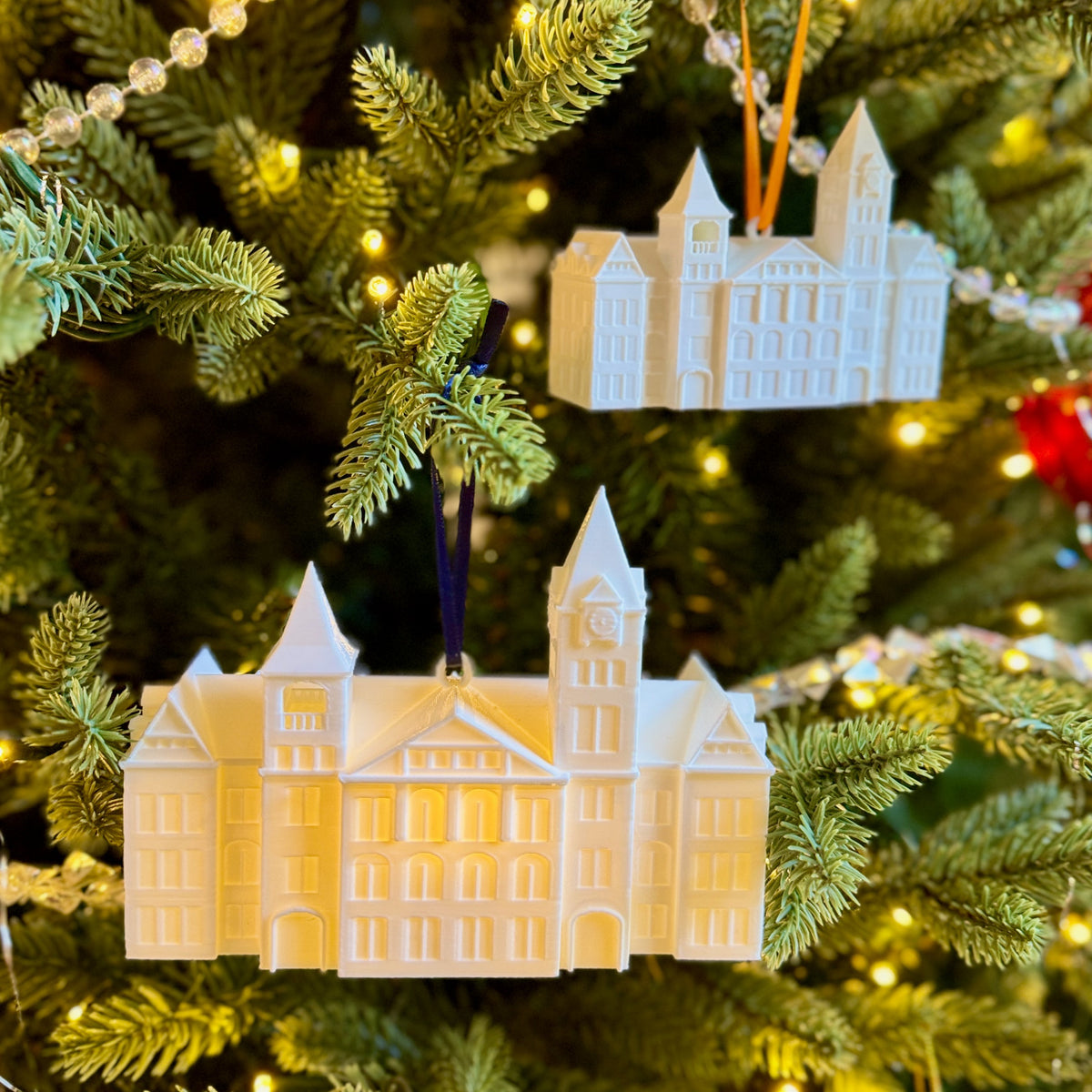Illuminated Auburn Samford Hall ornament hanging on a decorated Christmas tree, used as a holiday alumni gift.