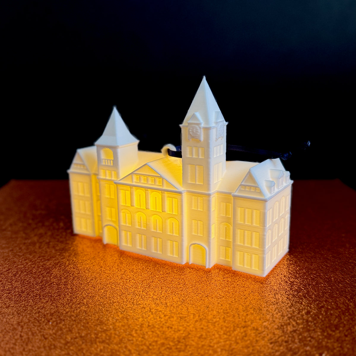 Glowing LED Auburn ornament of Samford Hall in dark setting — cozy college-themed holiday decor.
