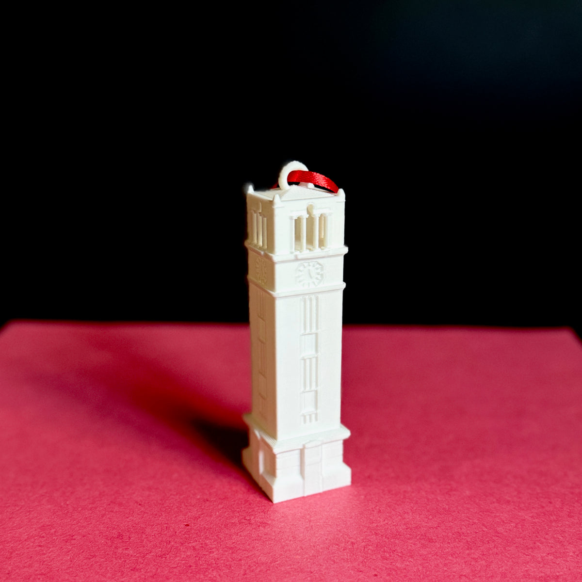 The NC State keepsake ornament of the Bell Tower on campus, shown against a red background.