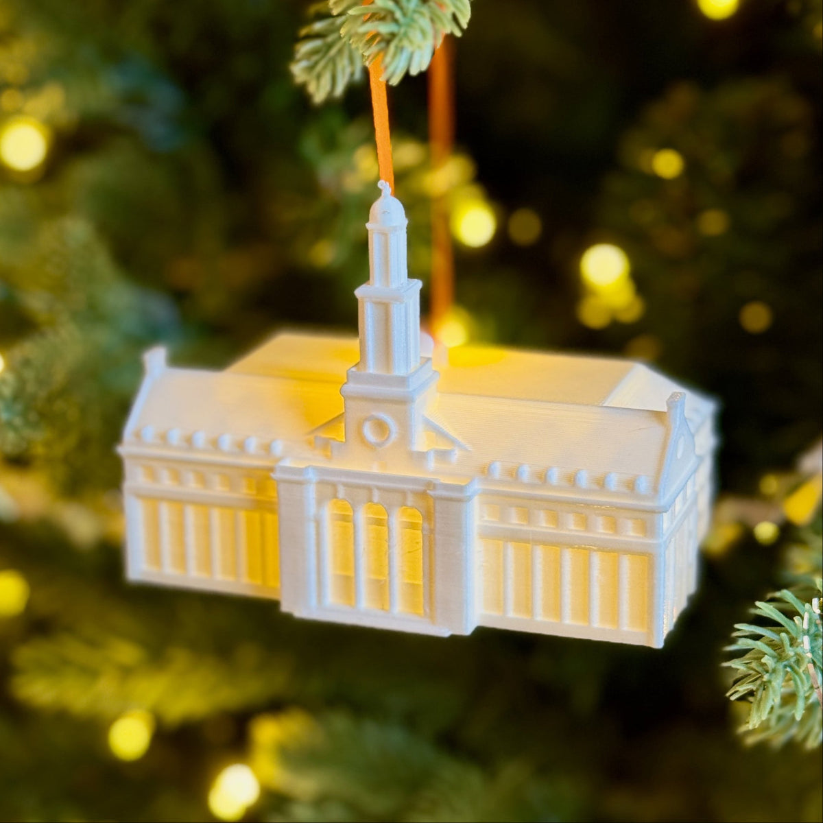 Illuminated Oklahoma State Edmon Low Library ornament hanging on a Christmas tree.