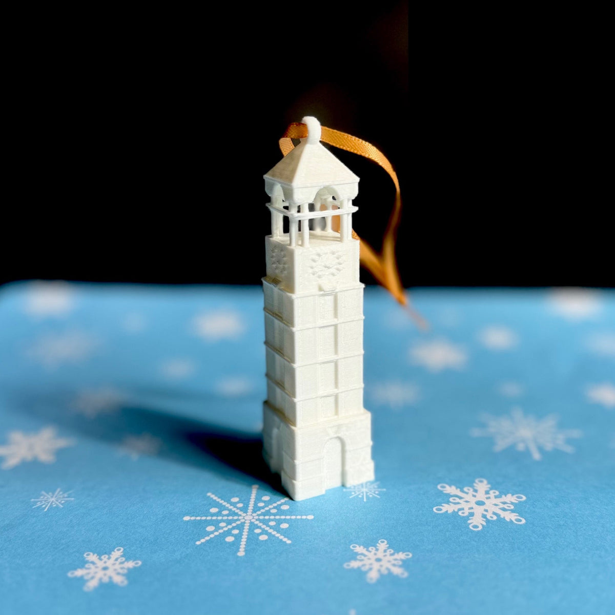 The Purdue Christmas ornament of the bell tower, shown on a blue holiday background.