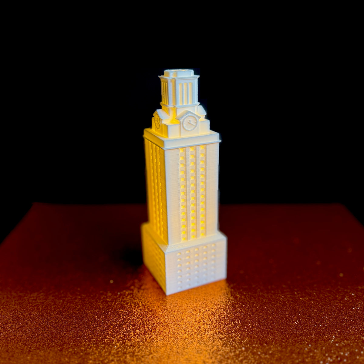 The UT Tower figurine, shown in white against an orange background. Ideal as Texas Longhorns decor.