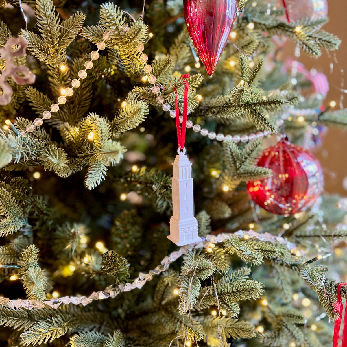 The Denny Chimes ornament for University of Alabama alumni, shown on a decorative Christmas tree with ornaments and lights
