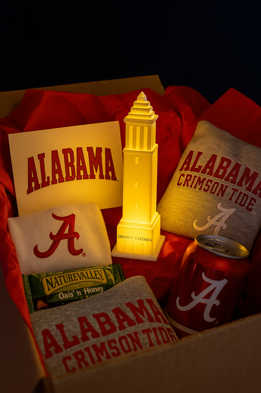 University of Alabama care package with red tissue paper, featuring a glowing LED Denny Chimes figurine, Alabama-themed shirts, a greeting card, a Nature Valley granola bar, and a red soda can with the Alabama 'A' logo.