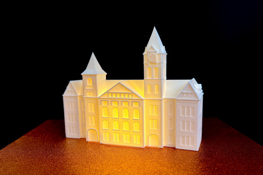 3D printed LED lighted figurine of Auburn University’s Samford Hall, glowing warmly with detailed architecture including towers, clock face, and arched windows, displayed on a textured surface.