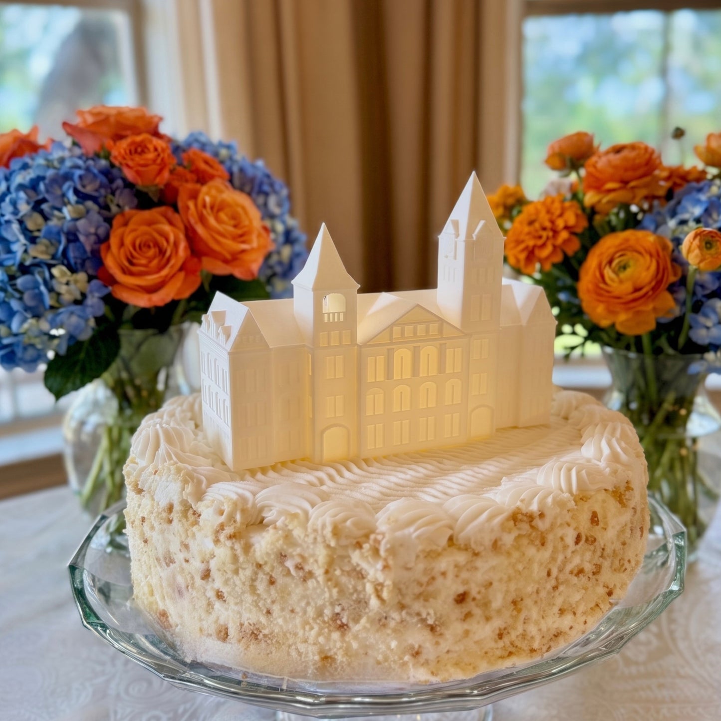Auburn University Samford Hall 3D lighted figurine used as a cake topper at a wedding on a white cake, surrounded by blue and orange floral arrangements.