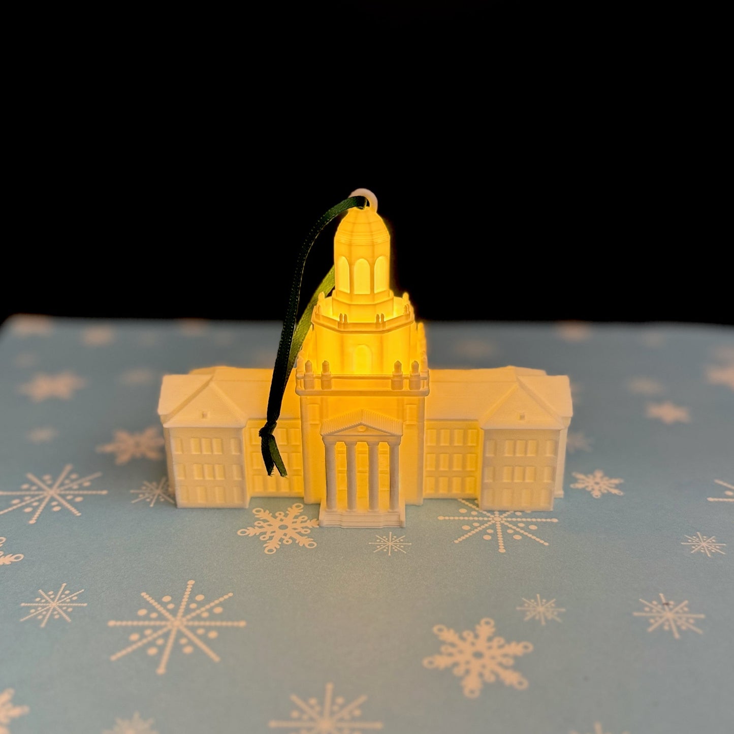 Warm LED light illuminating from within a 3D-printed Pat Neff Hall ornament in a dark setting.