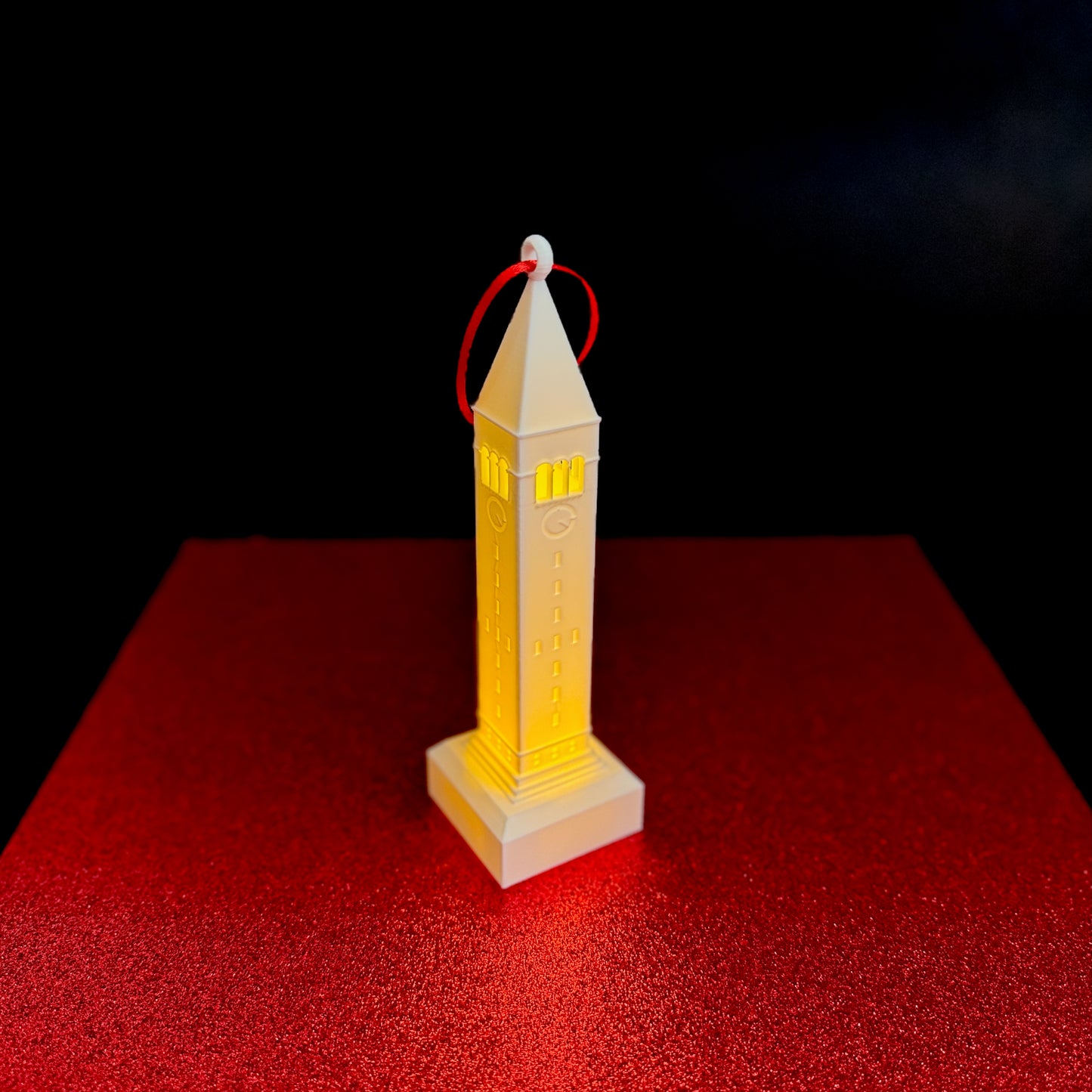 The Cornell Tower ornament with an LED light, shown against a red background.