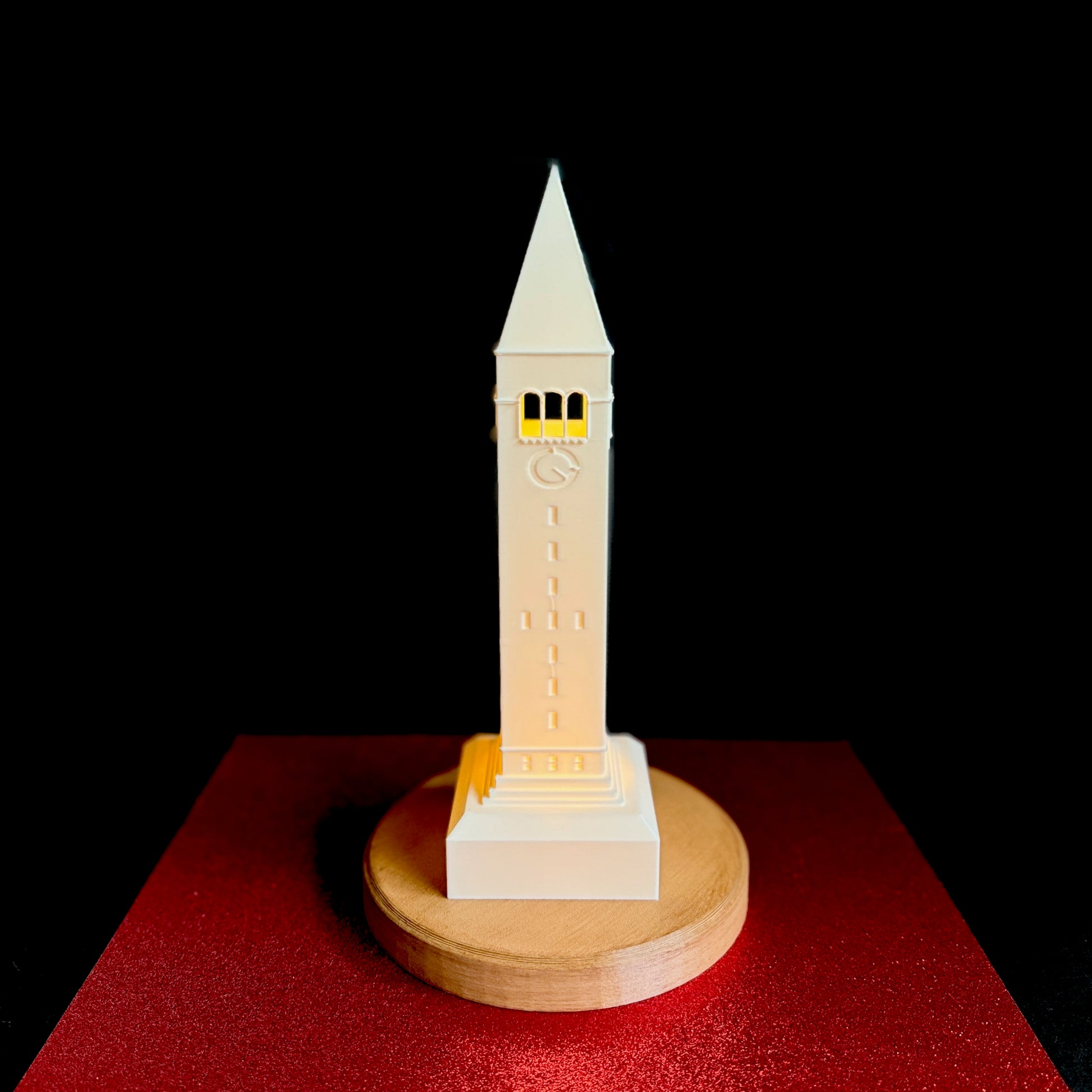 Front view of the Cornell University light, shown against a red background and designed as the McGraw Bell Tower.