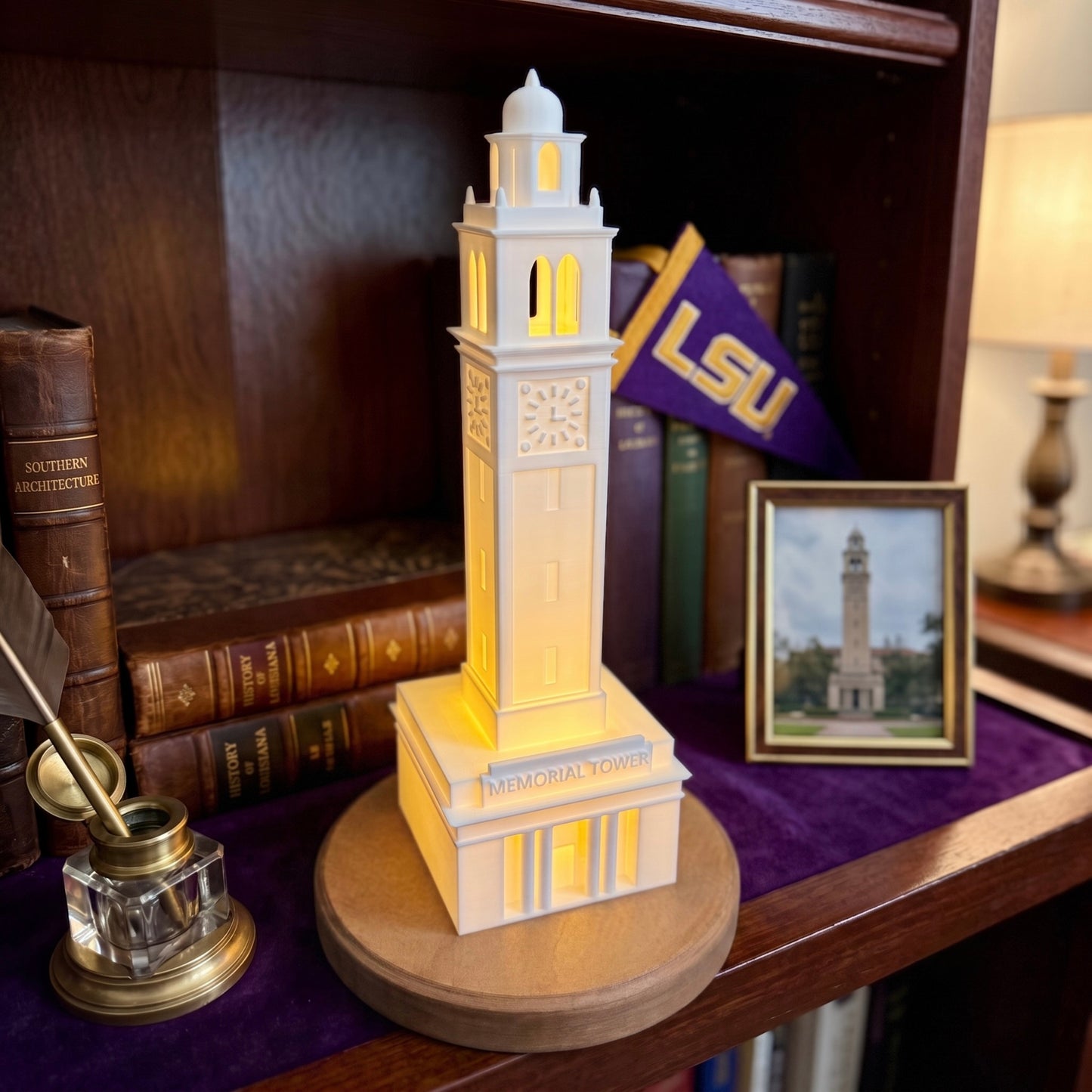 A glowing LSU Memorial Tower LED desk light sitting on a purple velvet shelf, surrounded by antique books, a vintage inkwell, and a miniature LSU pennant.