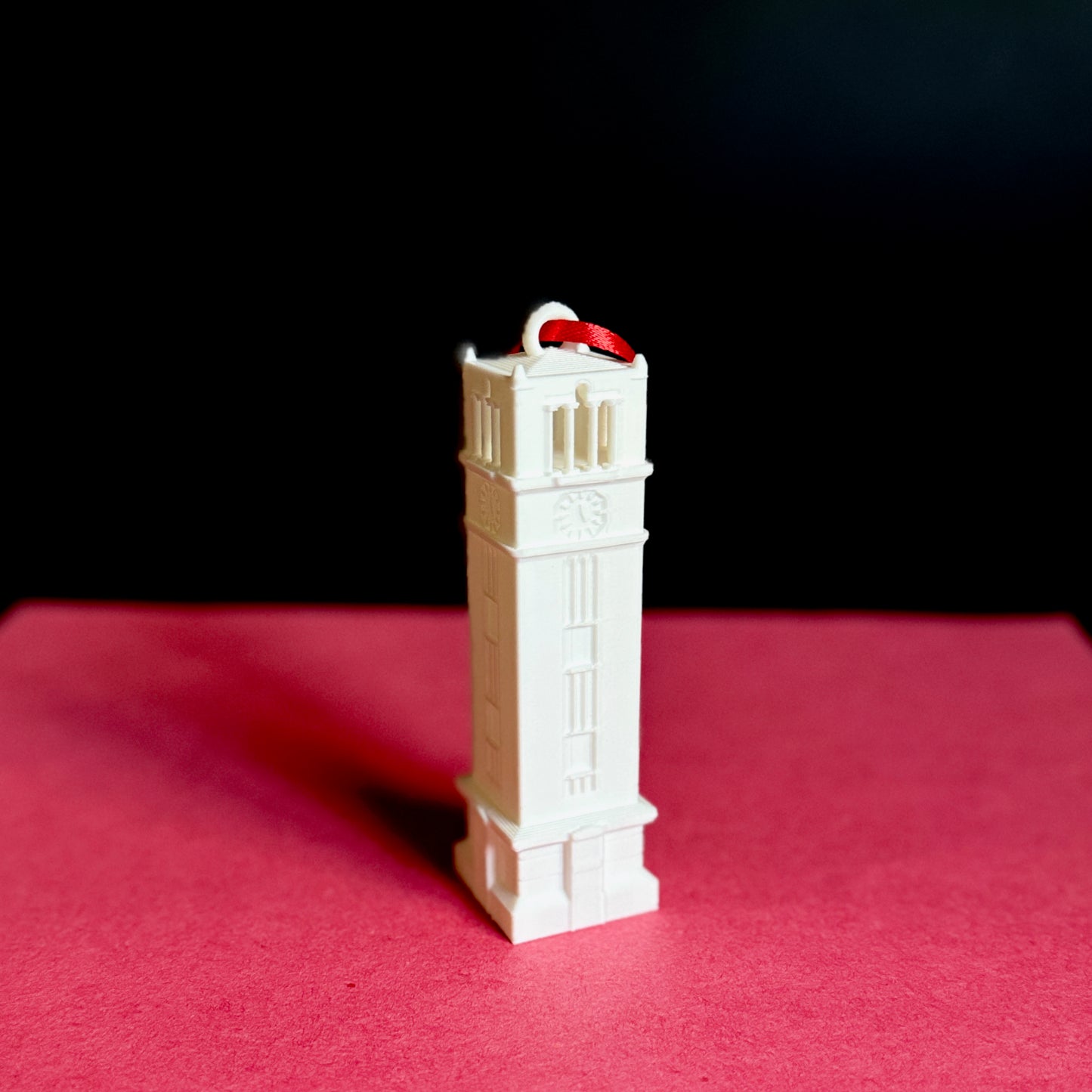 The NC State keepsake ornament of the Bell Tower on campus, shown against a red background.