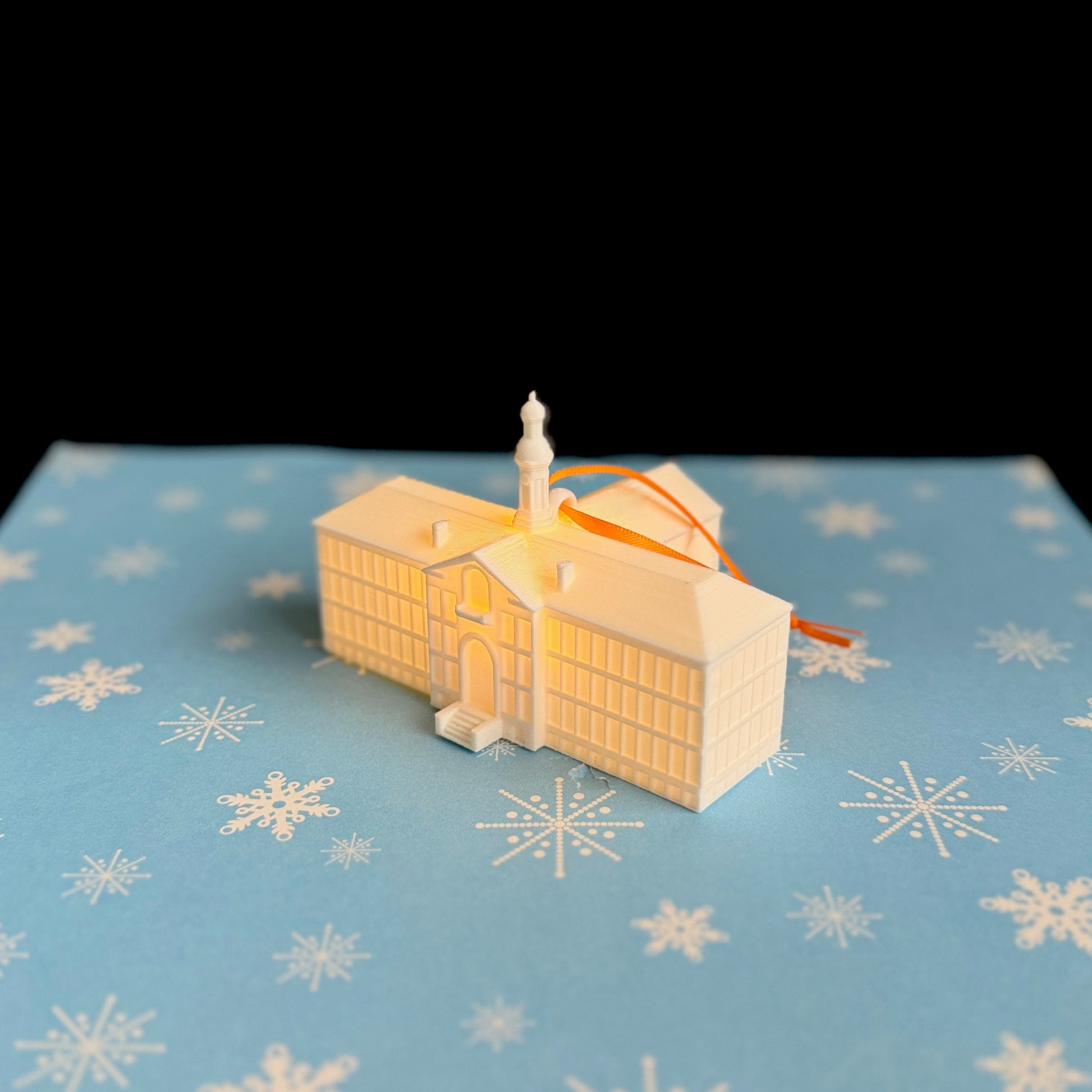 The Princeton Christmas ornament of the Nassau Hall building on campus, tied with an orange ribbon.