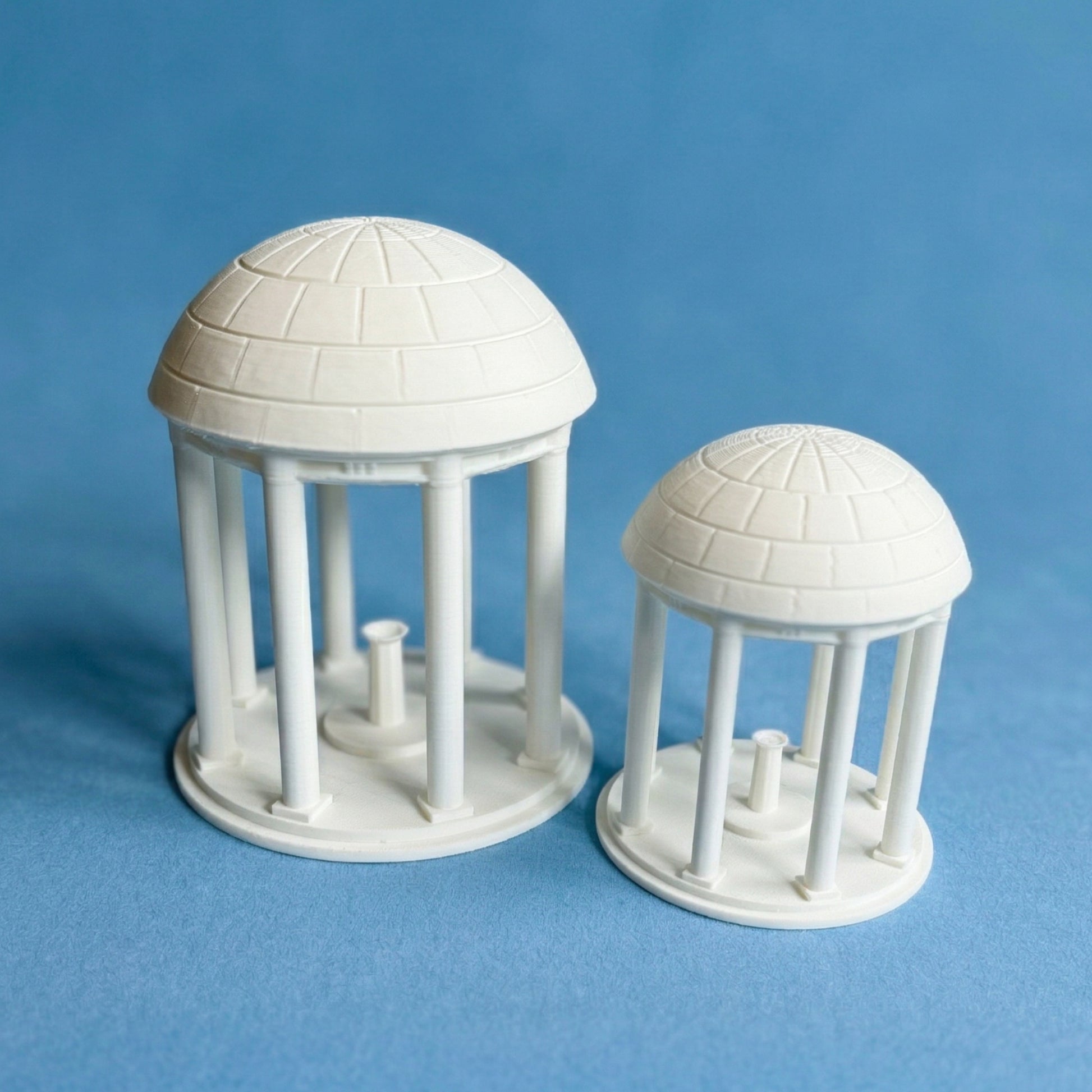 The UNC Old Well figurines, shown in detail against a Carolina Blue background.