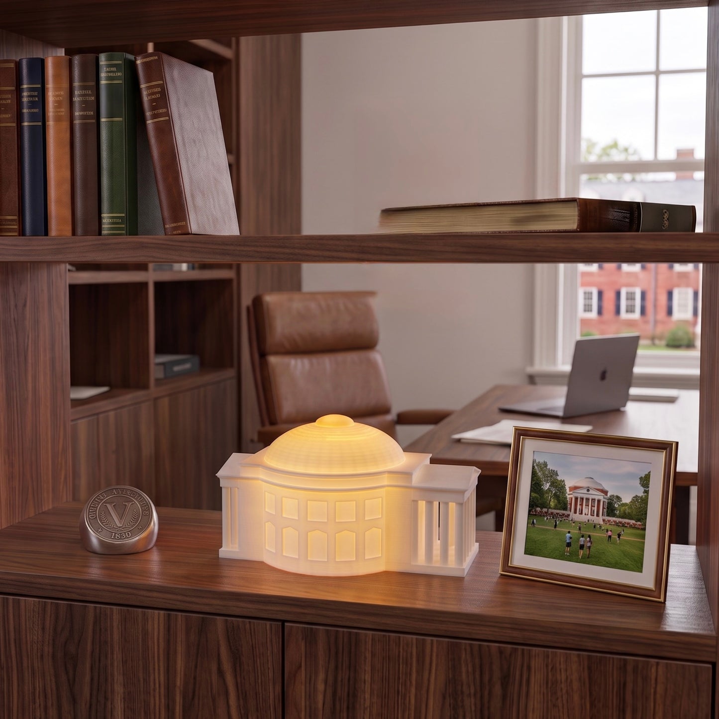 A miniature illuminated replica lamp of the UVA Rotunda, glowing warm white on a wooden shelf in an office of a UVA Alumni, next to a framed photo of the University of Virginia campus.