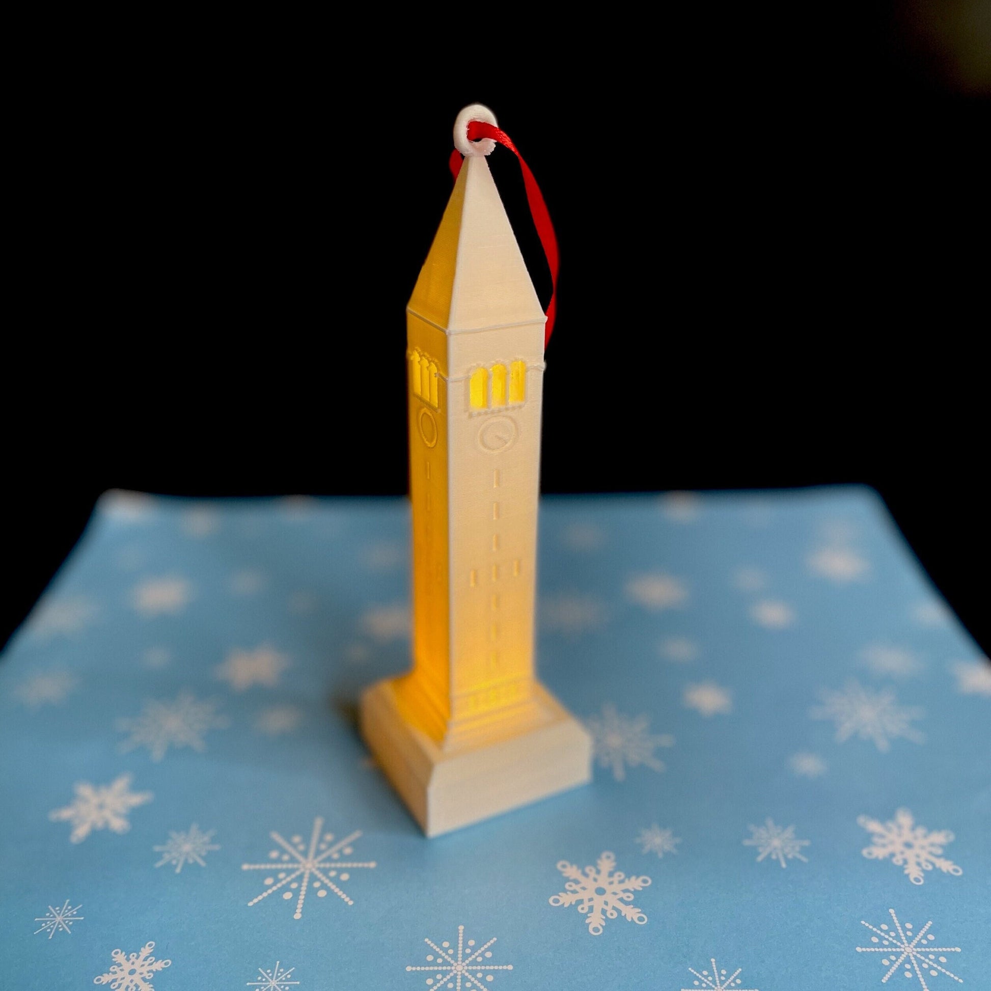 The Cornell ornament with a light, shown against a blue holiday background.